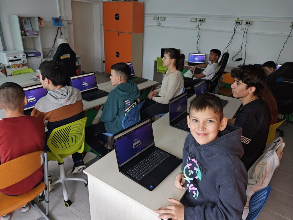 Elev care zâmbește pentru cameră în laboratorul de informatică, alături de colegi