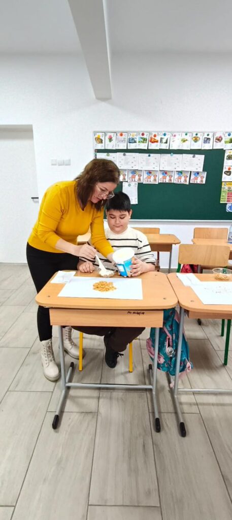 Doamna profesoară îl ajută pe elev să taie piersici