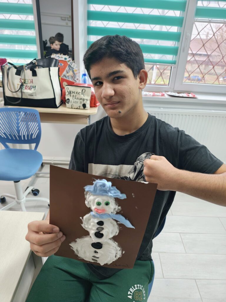 Un elev a realizat un om de zăpadă folosind spumă. Culori: alb, bleu, nasturi negri, nas portocaliu