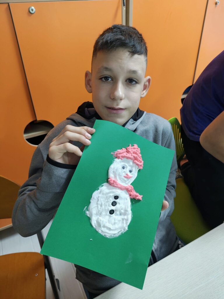 Elev arată omul său de zăpadă cu fes și fular roșu