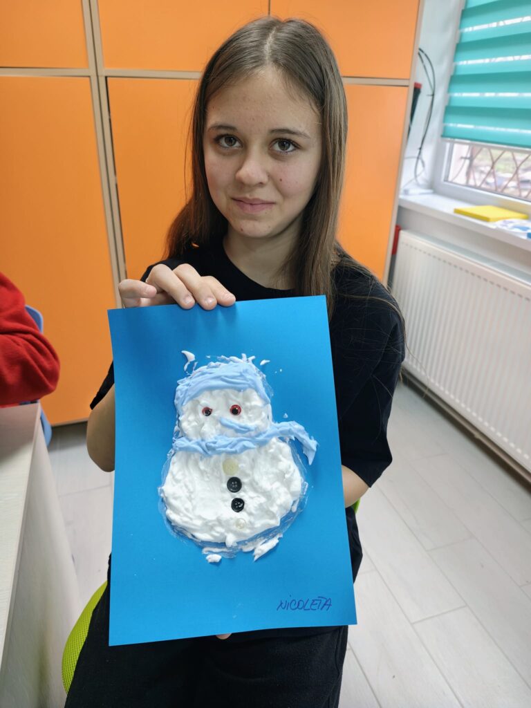 Elevă prezintă omul de zăpadă din spumă cu fular și fes albastru.
