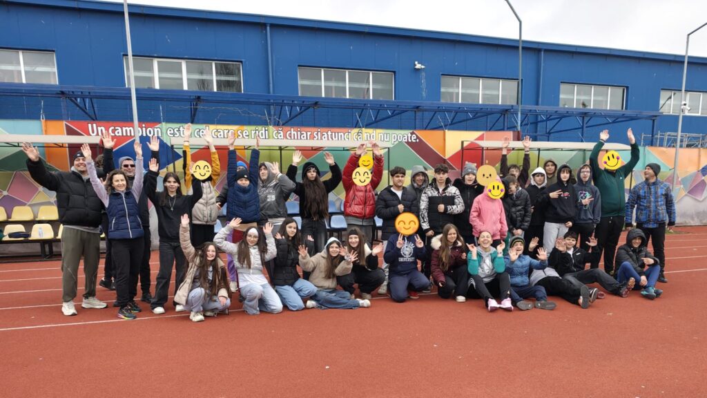 Poză cu grupul complet, elevi, profesori și părinți, bucuroși cu mâinile ridicate.