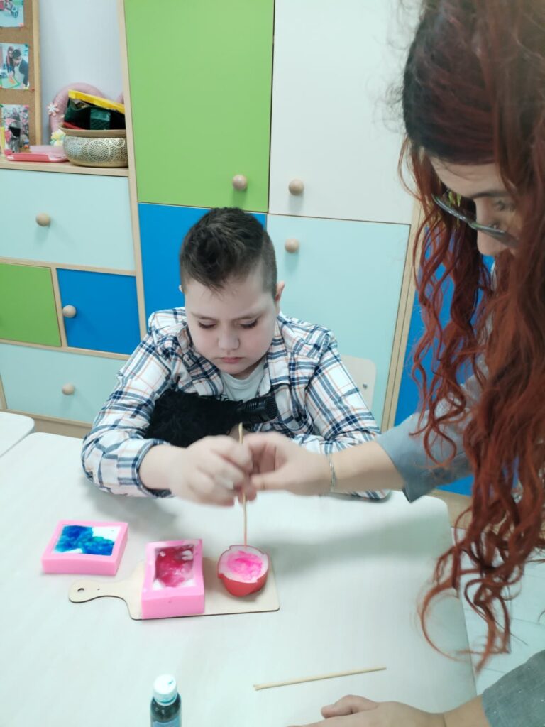 elevul sprijinit de profesoară amestecă ceara în formă