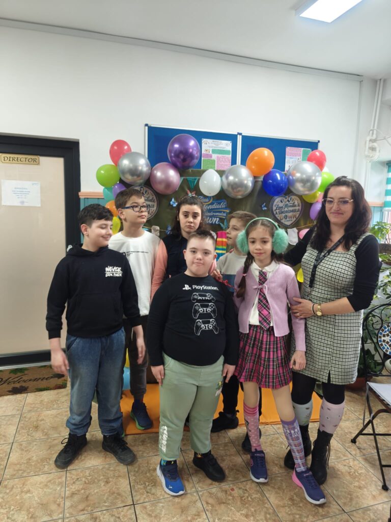 Doamna profesoară și elevii ei pozează în fața panoului