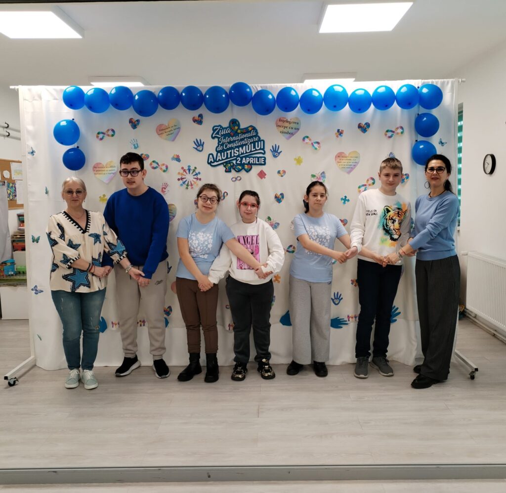 Doamnele profesoare și elevii se țin de mână în fața panoului