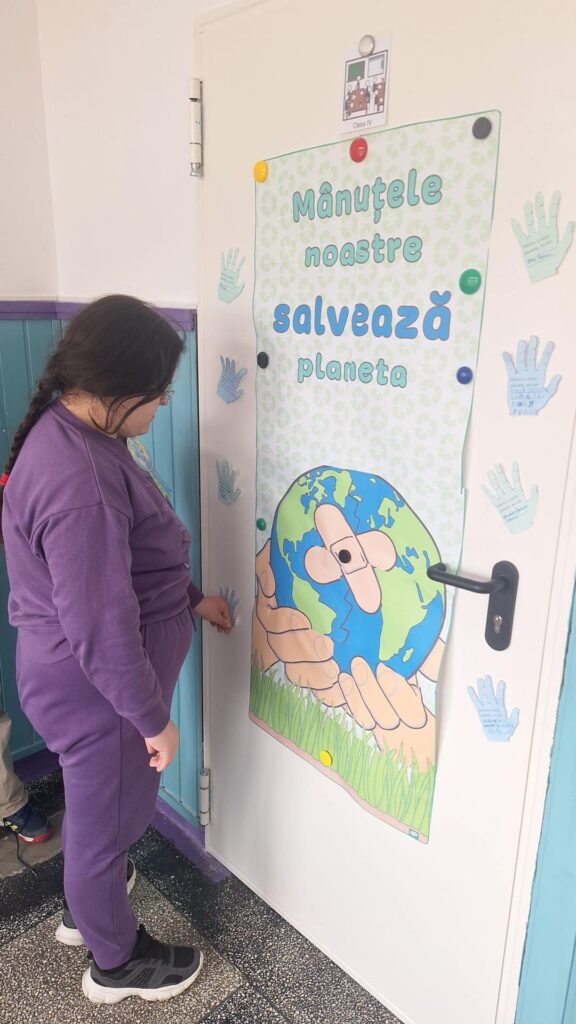 elevă lângă ușă pe care este lipit afișul realizat - Mânuțele noastre salvează planeta