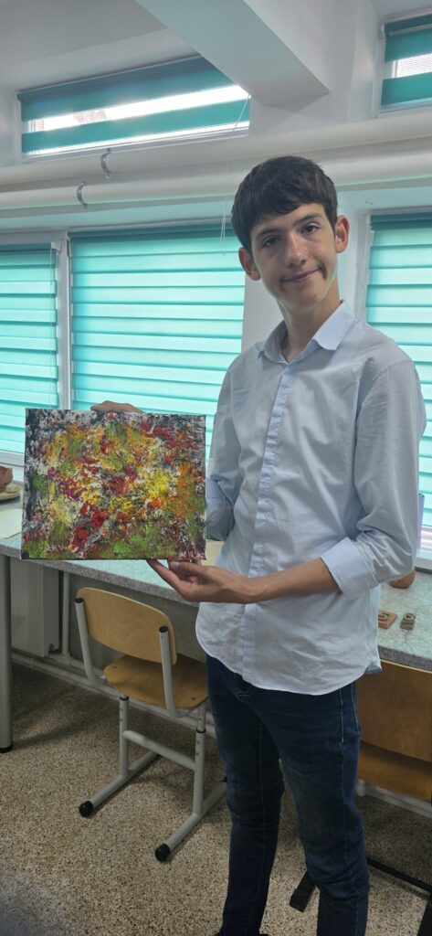 Elevul arată planșa pictată folosind galben, roșu, verde