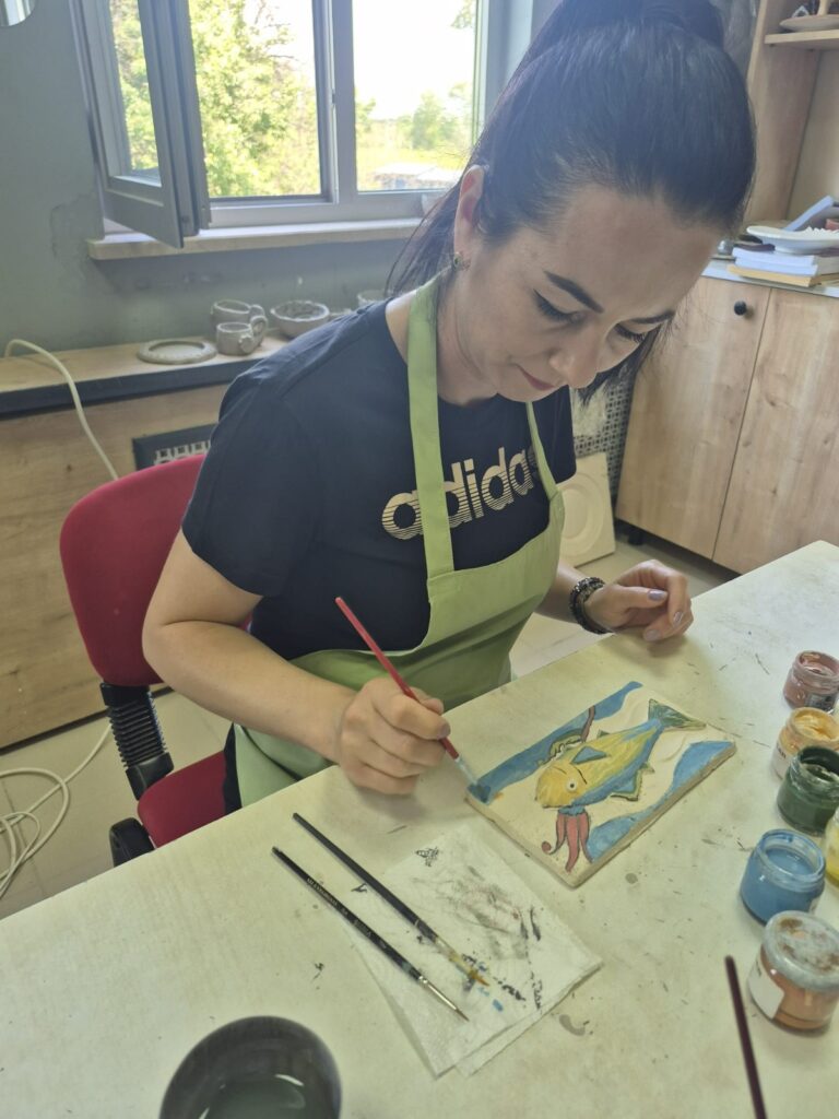 Doamna profesoară realizează o lucrare decorativă cu un pește colorat galben cu albastru
