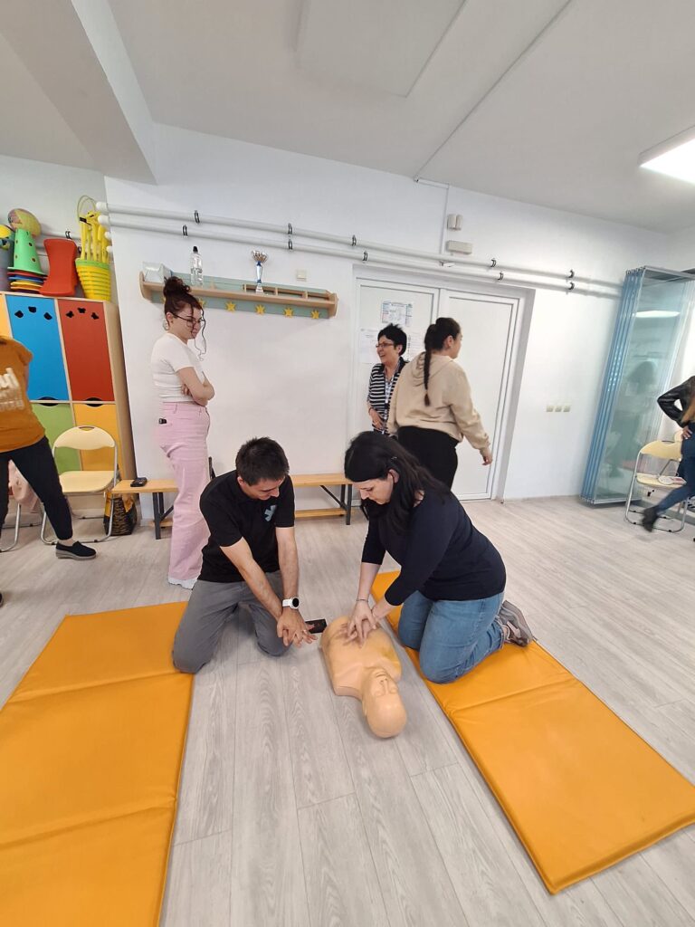profesoara realizează masaj cardiac manechinului sprijinită de trainer