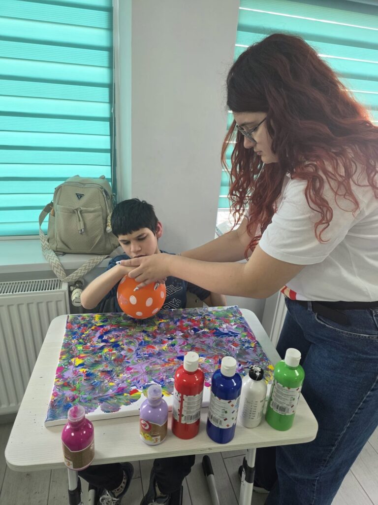 Doamna profesoară ajută elevul să își termine pictura pe canva.