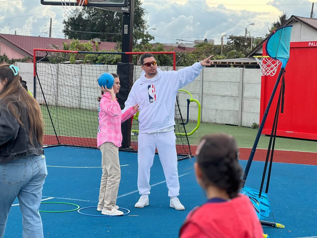 Domnul profesor arată elevei cum să arunce mingeae către coșul de baschet