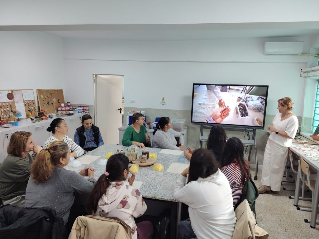 Imagine cu părinții ce urmăresc un video instructiv pe tabla interactivă din atelierul de lut