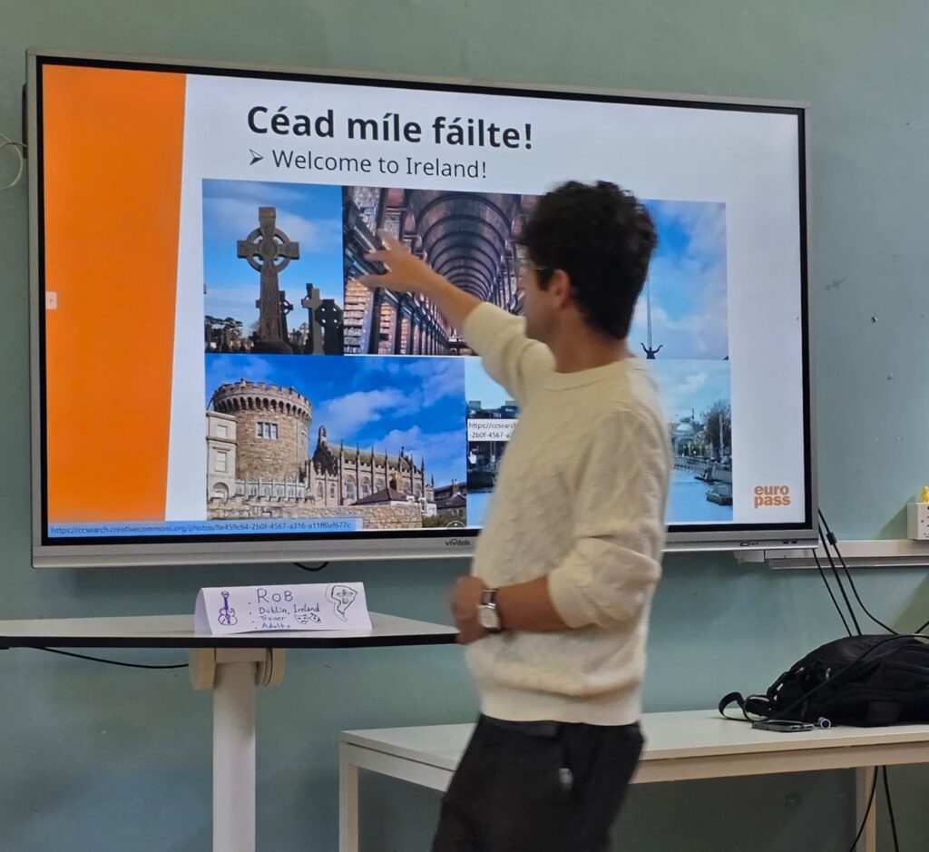 Formatorul cursului Europass Teacher Academy arată spre un ecran cu mesajul „Céad míle fáilte! Welcome to Ireland!” și imagini cu monumente din Dublin, în prima zi a cursului.