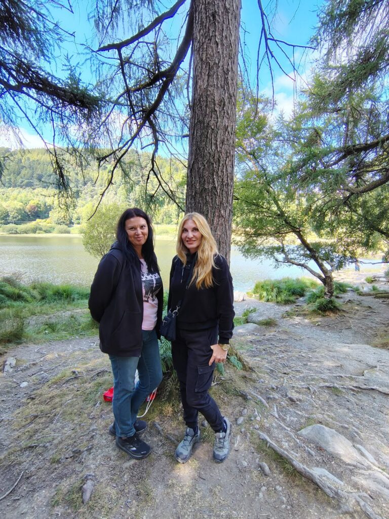 Cele două profesoare pe malul unui lac înconjurat de păduri, în vizita la Glendalough.