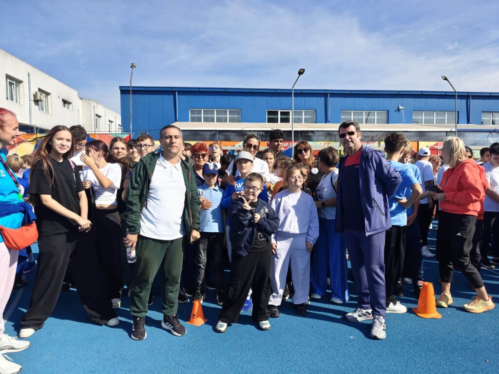 Elevi și profesori de la mai multe școli din Constanța pozează împreună pe terenul de sport; un băiat face semnul victoriei.