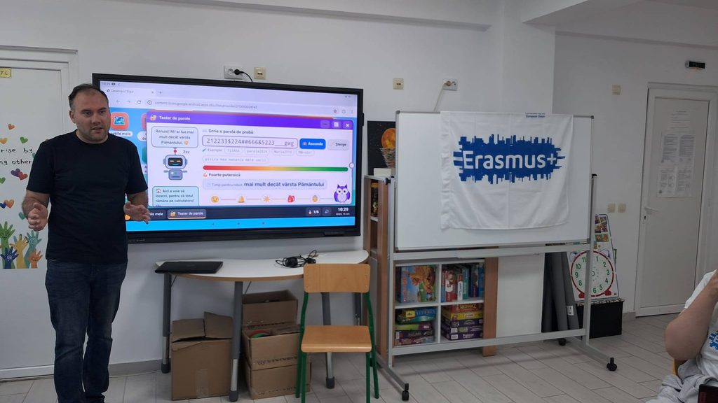 Un profesor prezintă un test de securitate pentru parole pe un ecran mare în cadrul unei sali de clasă. În fundal se observă un banner Erasmus+.