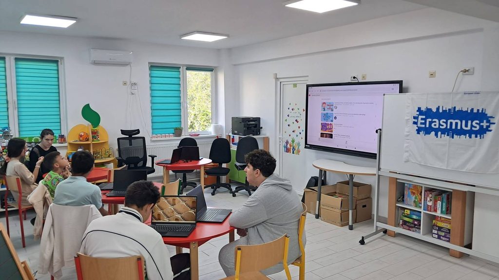  Un instructor interacționează cu un grup de elevi în timpul unui atelier despre siguranța în mediul online, utilizând echipamente computaționale.