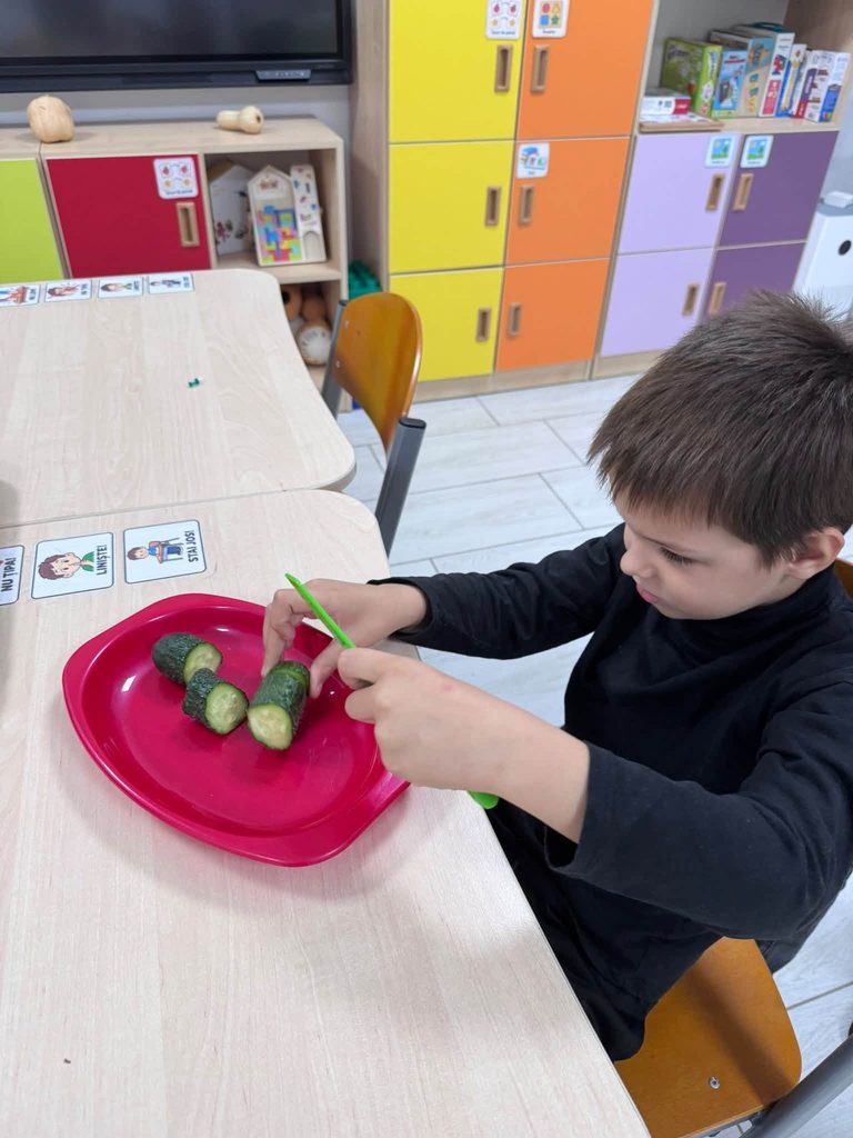 Un copil taie o felie de castravete de pe o farfurie roșie